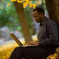 Man sitting under tree with laptop.